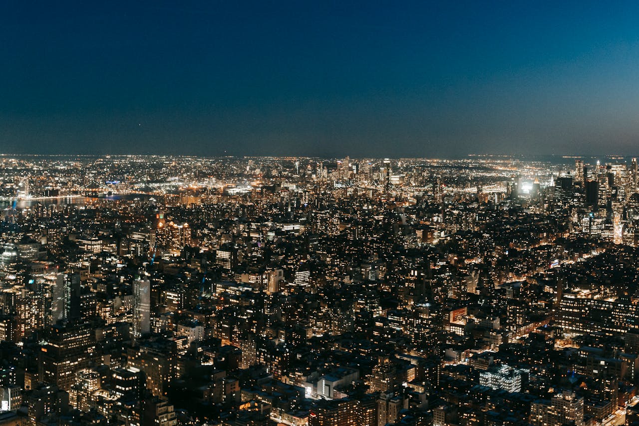 Modern buildings with glowing lights located on dark streets of contemporary densely built city against cloudless sky at night time